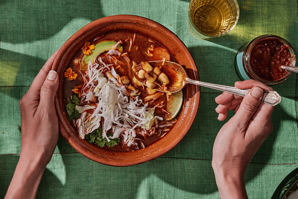 Bowl of pozole rojo topped with cabbage, avocado, cilantro, onions, and radishes