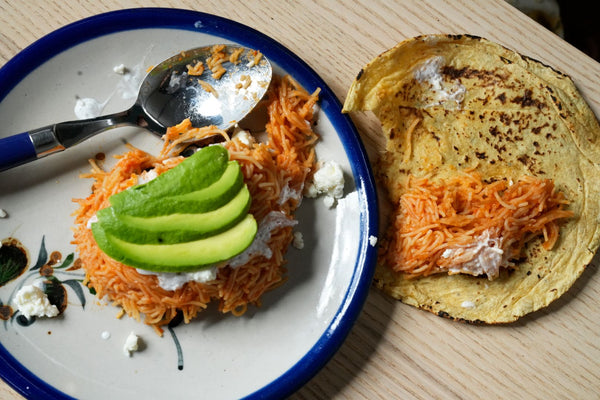 Plato de taco de sopa seca de fideo, cubierto con crema, queso fresco y aguacate