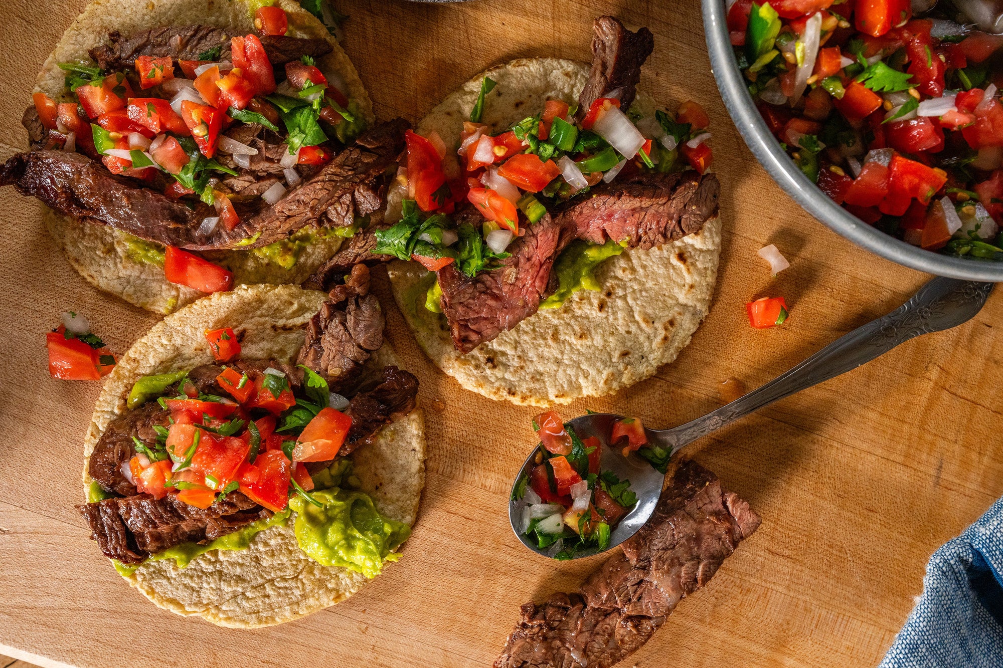 Tacos de asada con una capa de guacamole y cubiertos con pico de gallo