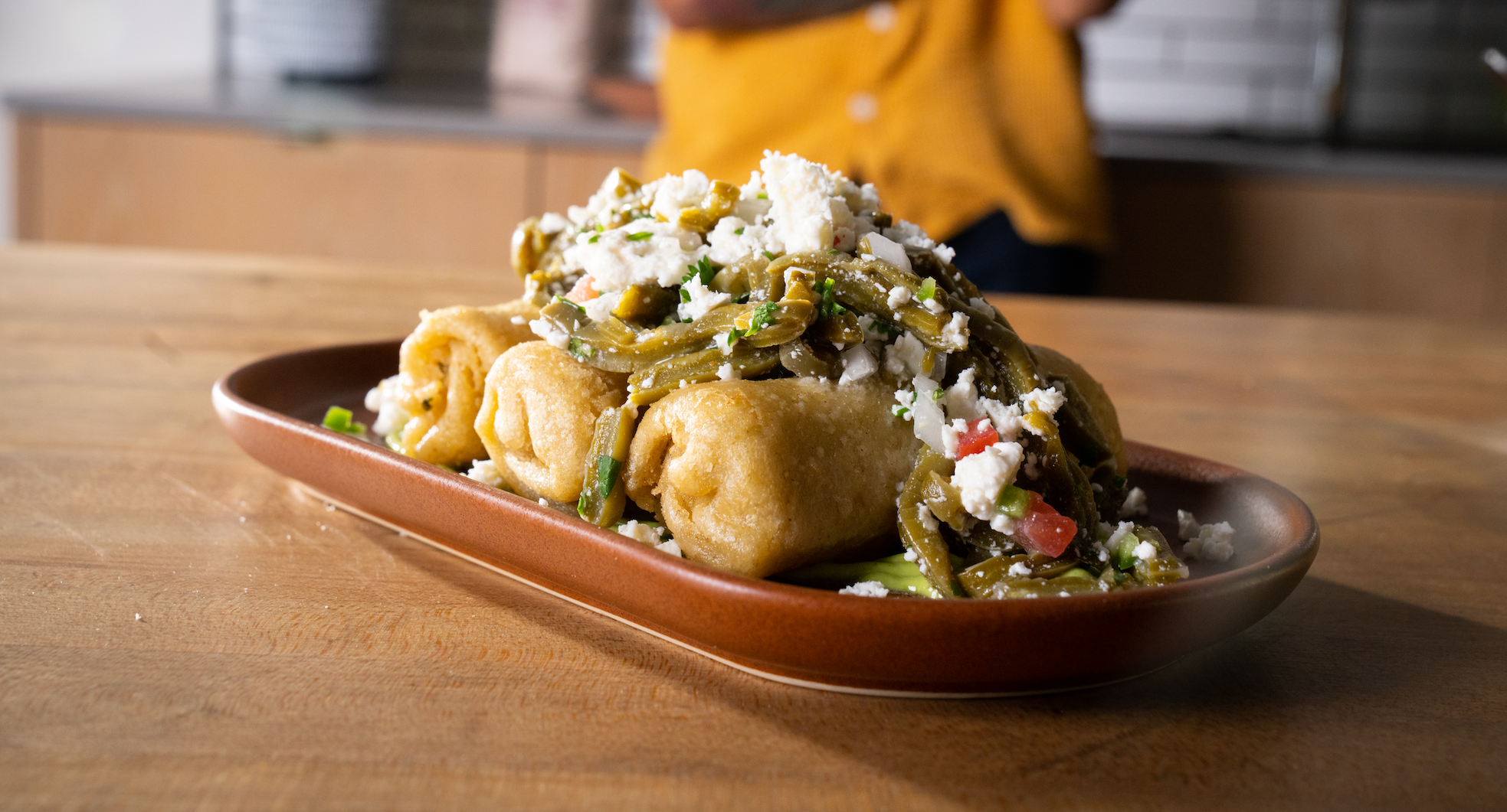 Un plato con pollo confitado y flautas de papa bañadas con salsa de nopales y queso