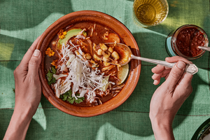 Bowl of pozole rojo topped with cabbage, avocado, cilantro, onions, and radishes