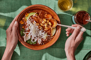 Bowl of pozole rojo topped with cabbage, avocado, cilantro, onionns, and radishes