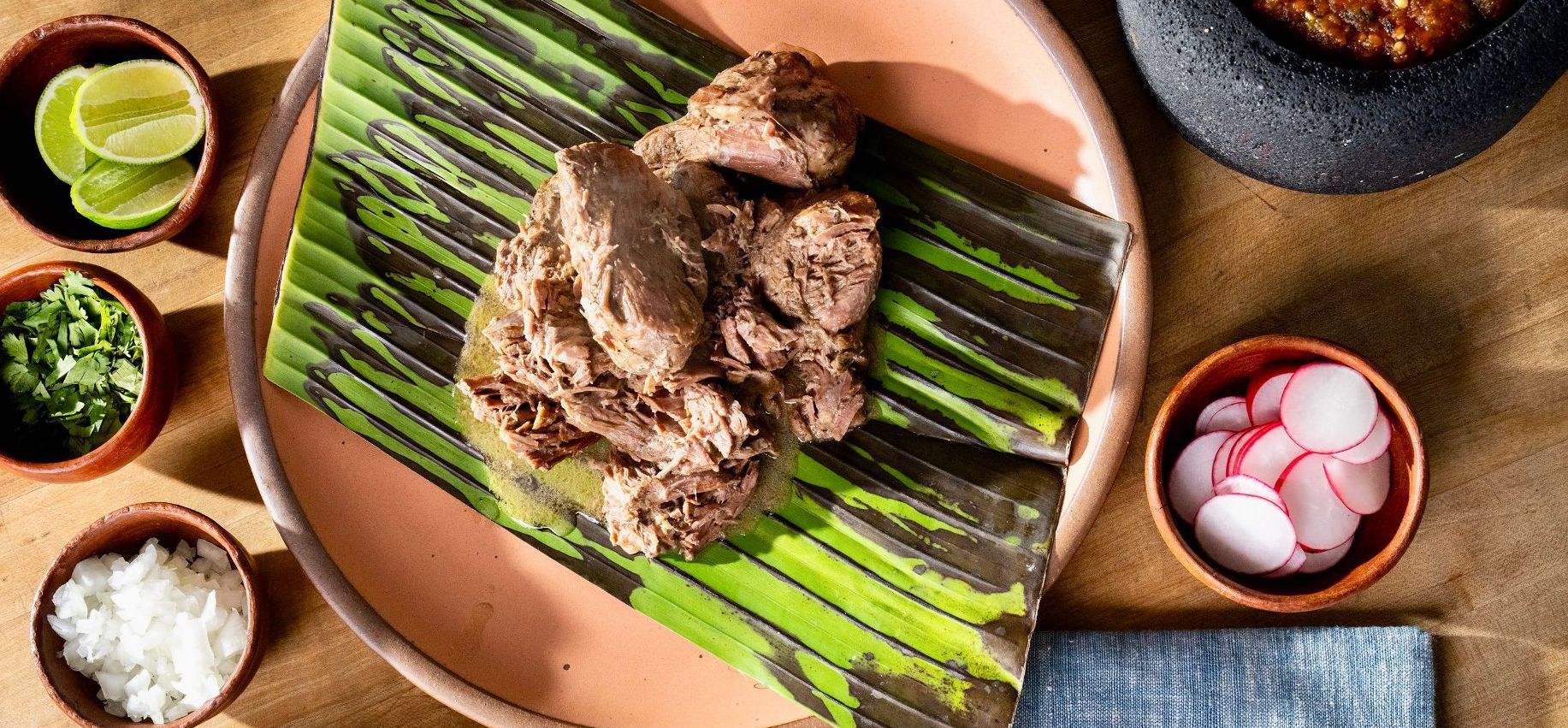 Lamb barbacoa alongside onion, cilantro, limes, radishes, and salsa.