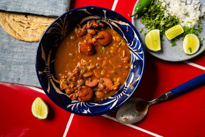 Bowl of frijoles charros (beans, broth, sausage) topped with cilantro, onion, lime, and served with tortillas