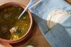 A bowl of albondigas alongside tortillas