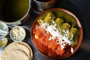 Plate of enchiladas divorciadas in red and green sauce topped with crema and queso fresco