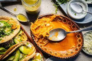 Plate of tinga alongside tacos de tinga topped with shredded lettuce, salsa, crema, queso, and avocado