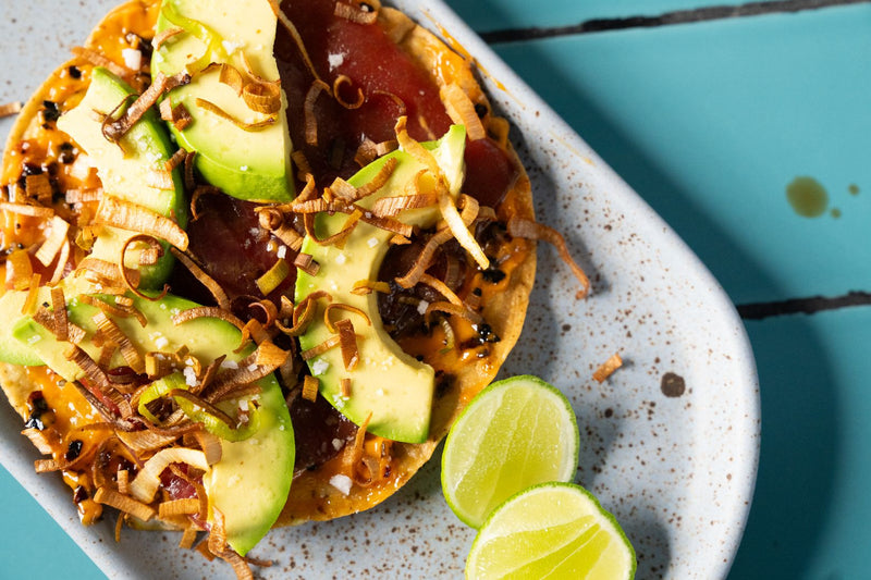 Tuna tostada topped with spicy mayo, fried leeks, avocado, and lime