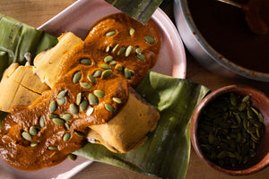Black bean and cheese tamales topped with mole sauce and roasted pumpkin seeds