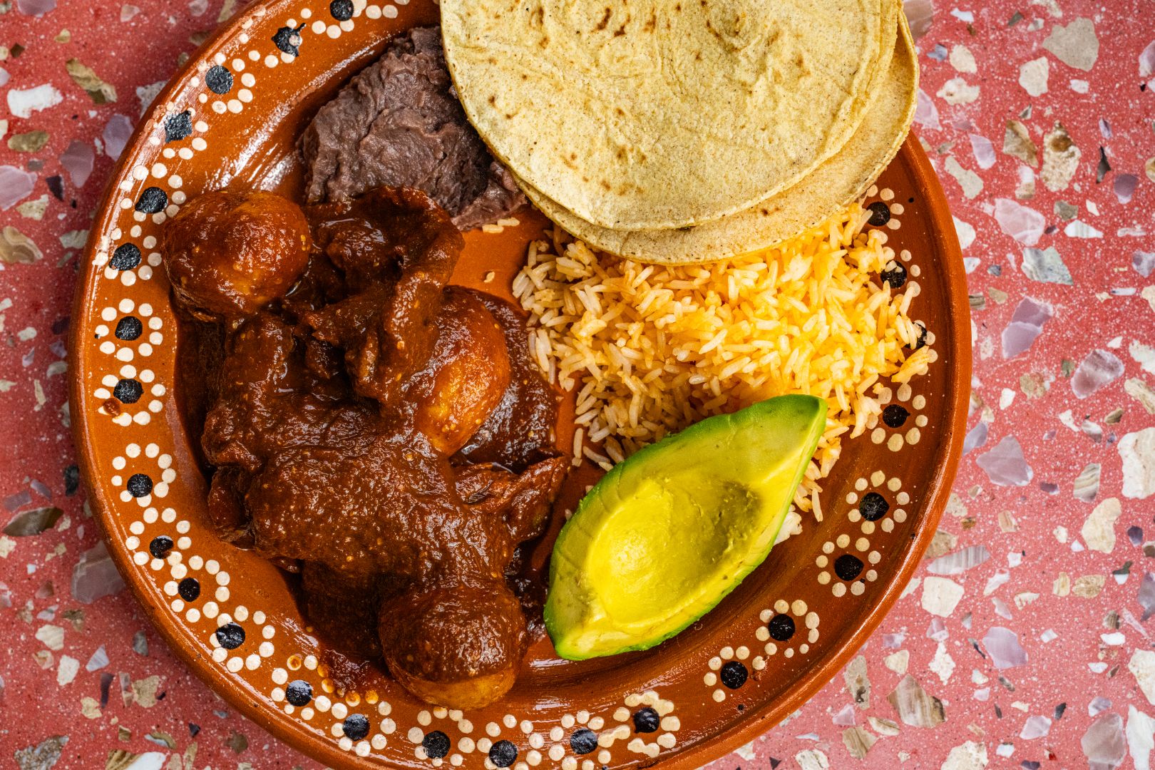 Bistec en pasilla served alongside rice, beans, avocado, and tortillas