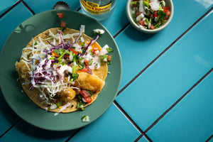 Plate of fish taco topped with cabbage, pico de gallo, and crema