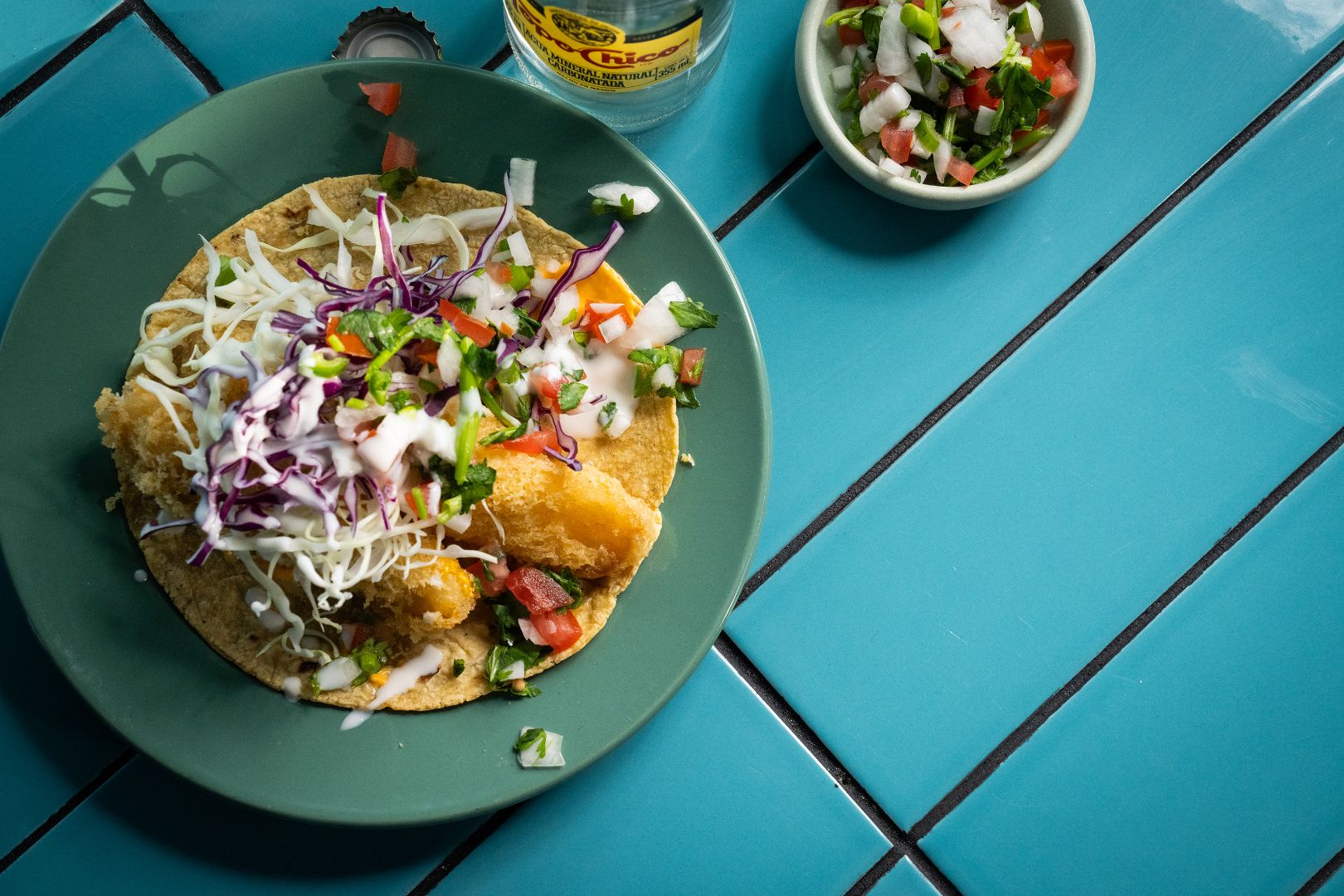 Plate of fish taco topped with cabbage, pico de gallo, and crema