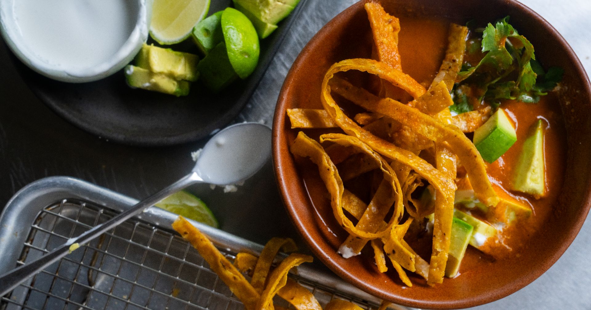 Bowl of tortilla soup with tortilla strips, avocado, cilantro, sour cream and lime