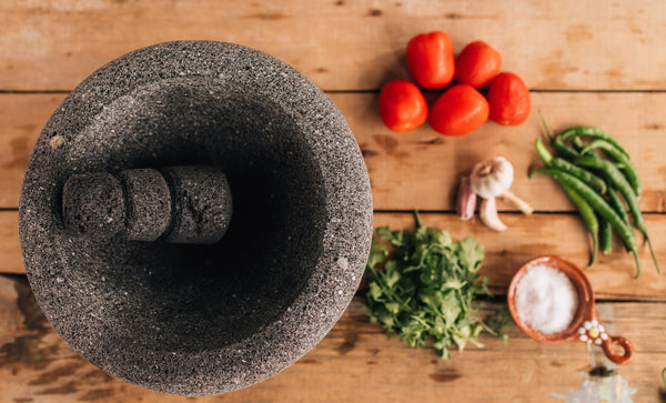 A molcajete with tomatoes, cilantro, garlic, peppers, and salt laid out