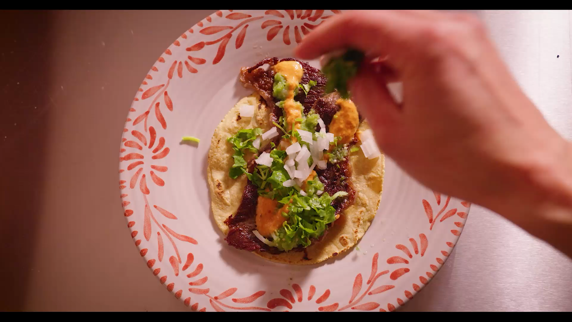 Mano añadiendo ingredientes a un taco en un plato decorativo